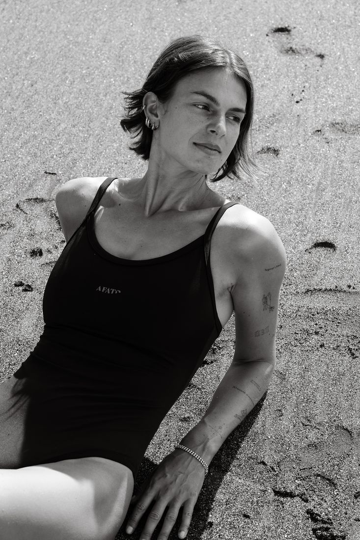 Black and white shot of a woman in a black swimsuit lying back on the sand