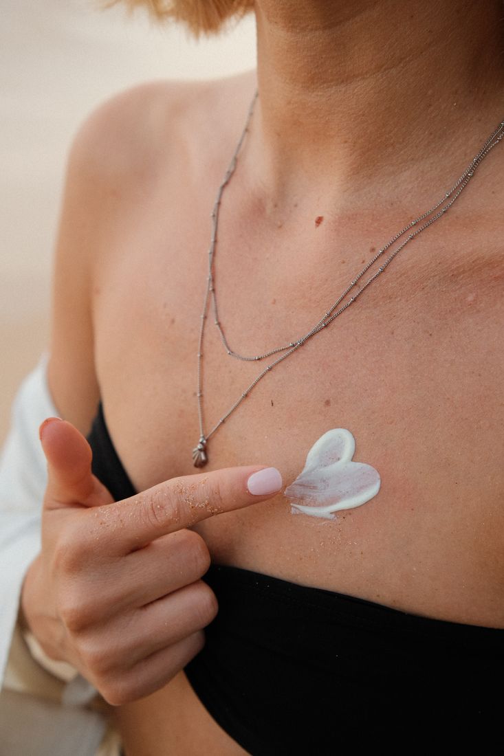 Close-up of a hand touching a pendant necklace, a heart of sun cream on the skin