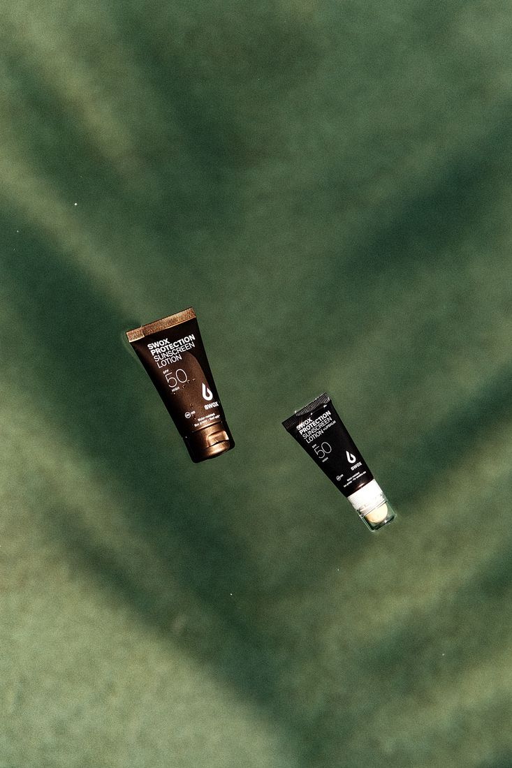 Two Swox sunscreen tubes floating on green water