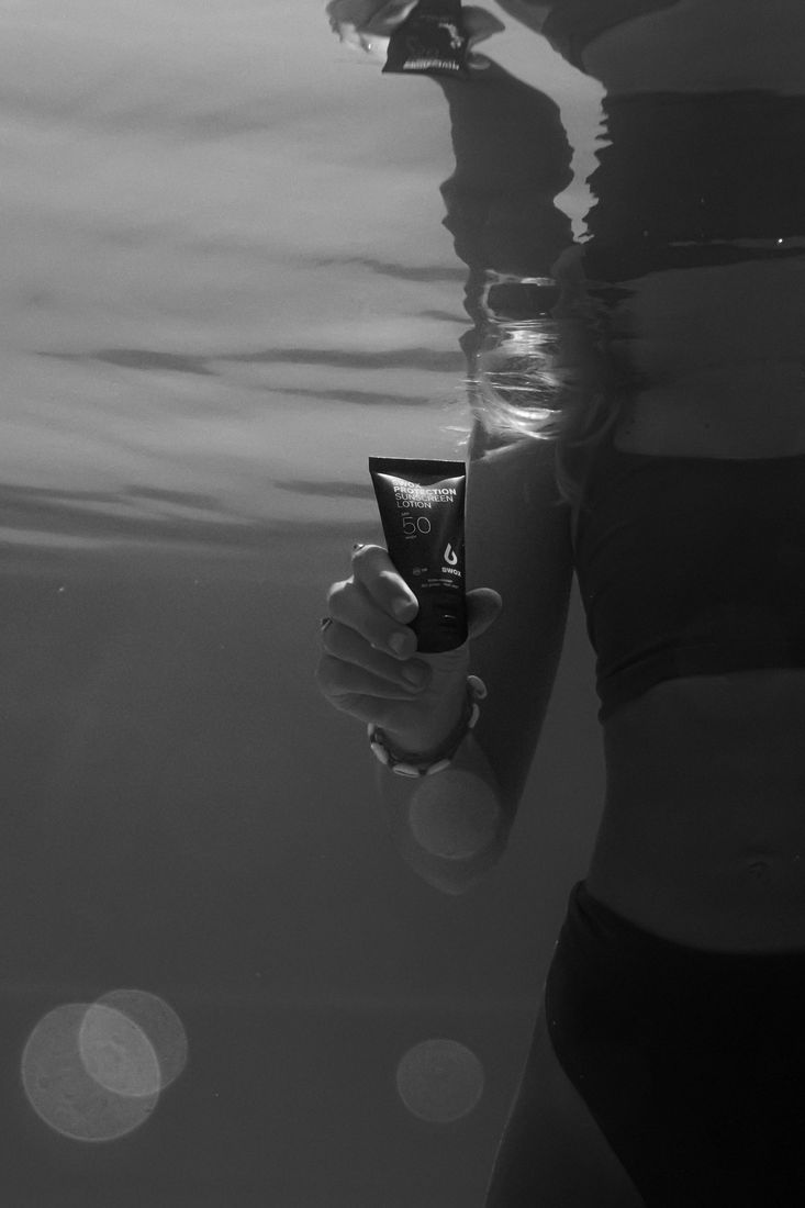 Black and white underwater shot of a swimmer holding a sunscreen tube