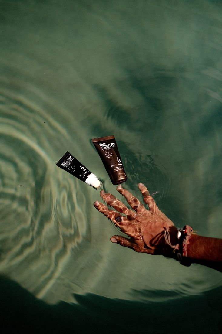 Hand reaching for two Swox sunscreen tubes on rippling green water