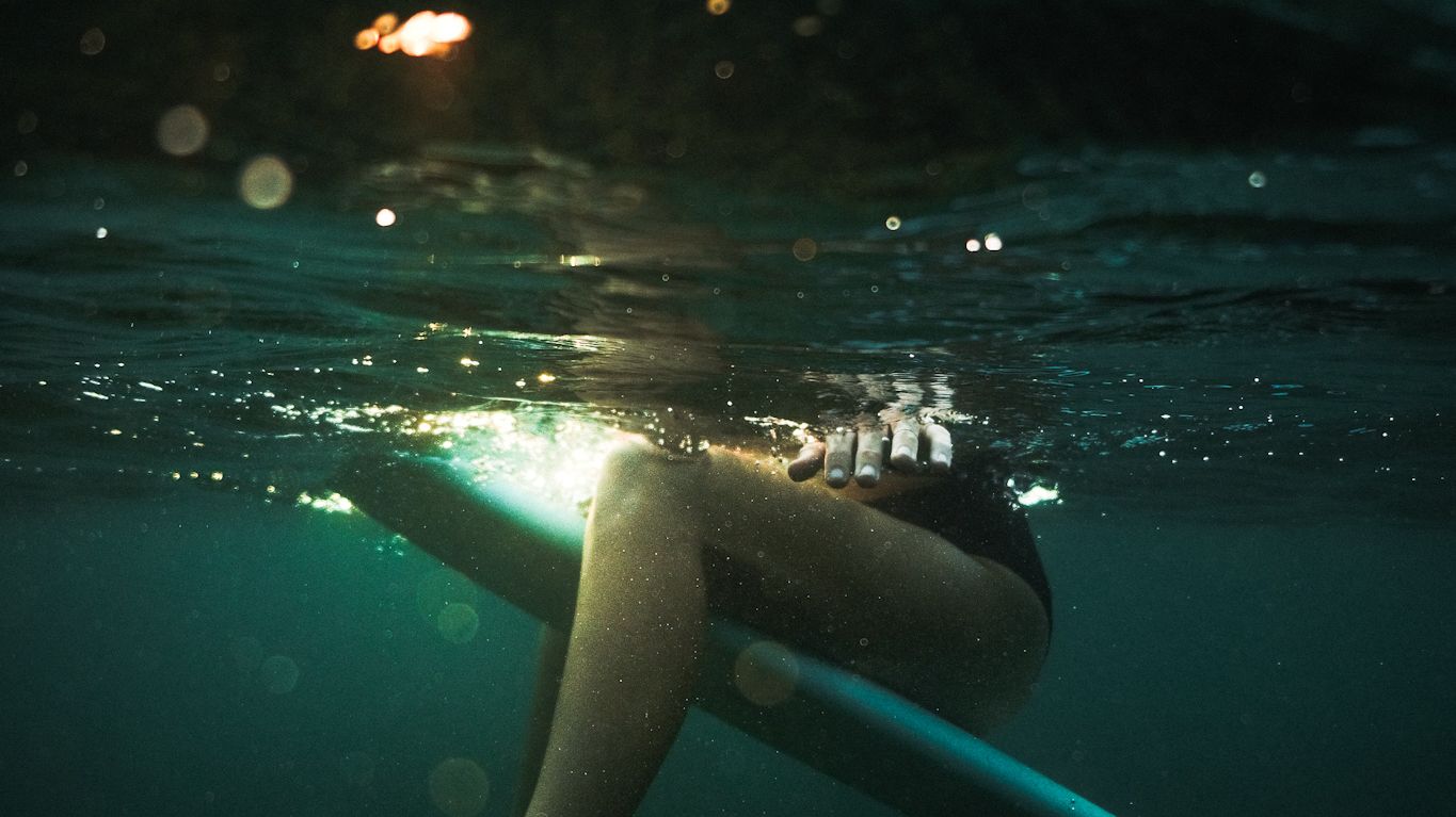 Underwater view of a surfer's legs resting on a board in teal water