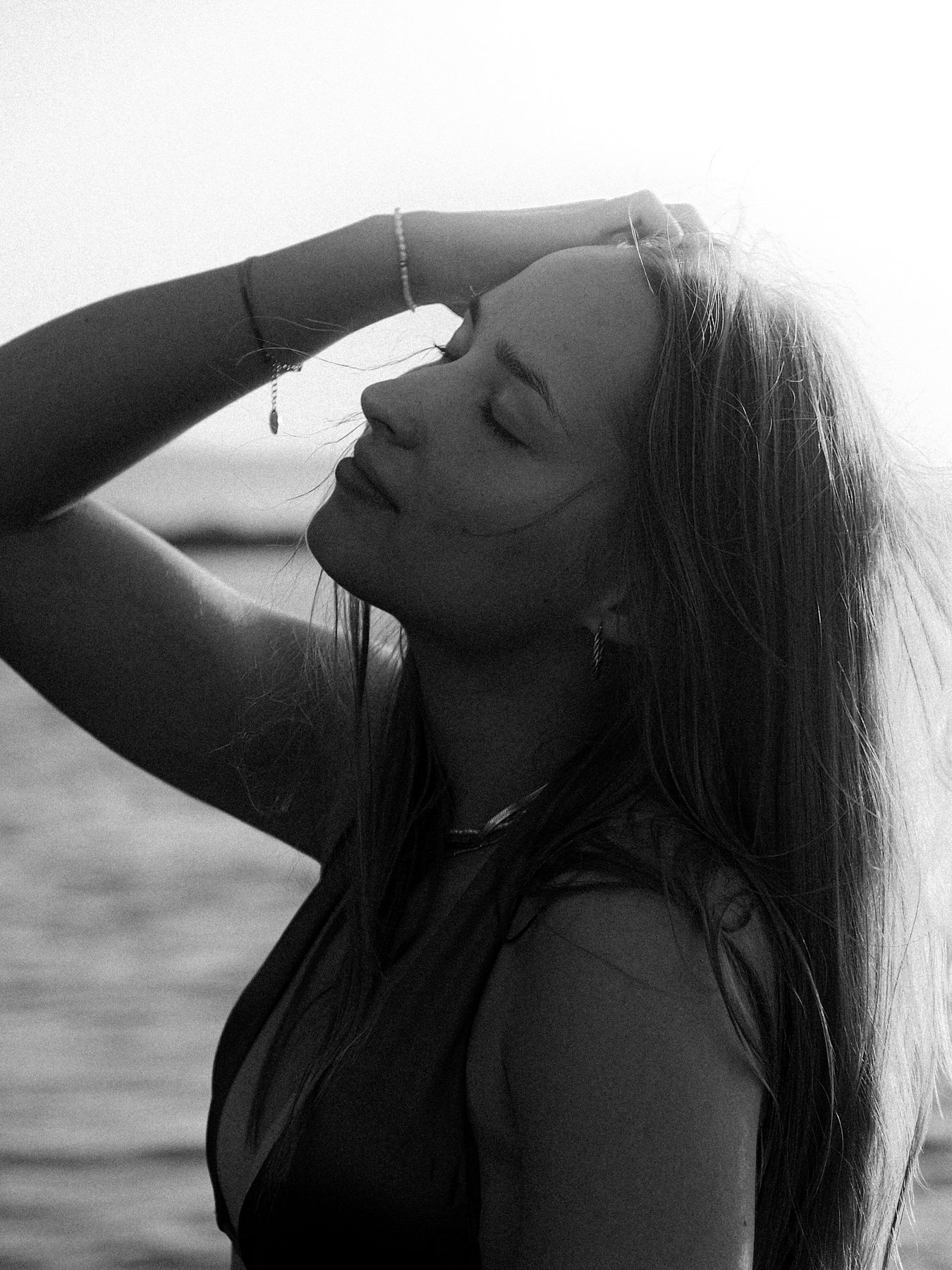 Black and white portrait of a woman with her hand in her hair, eyes closed, by the sea