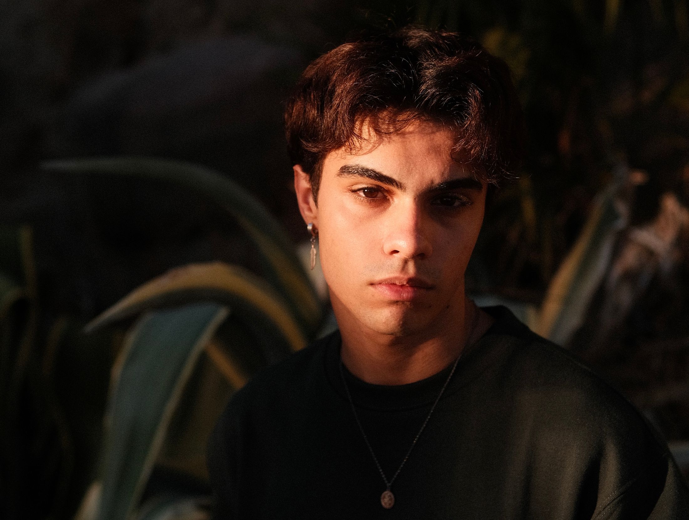 Young man with dark hair in warm evening light among green leaves