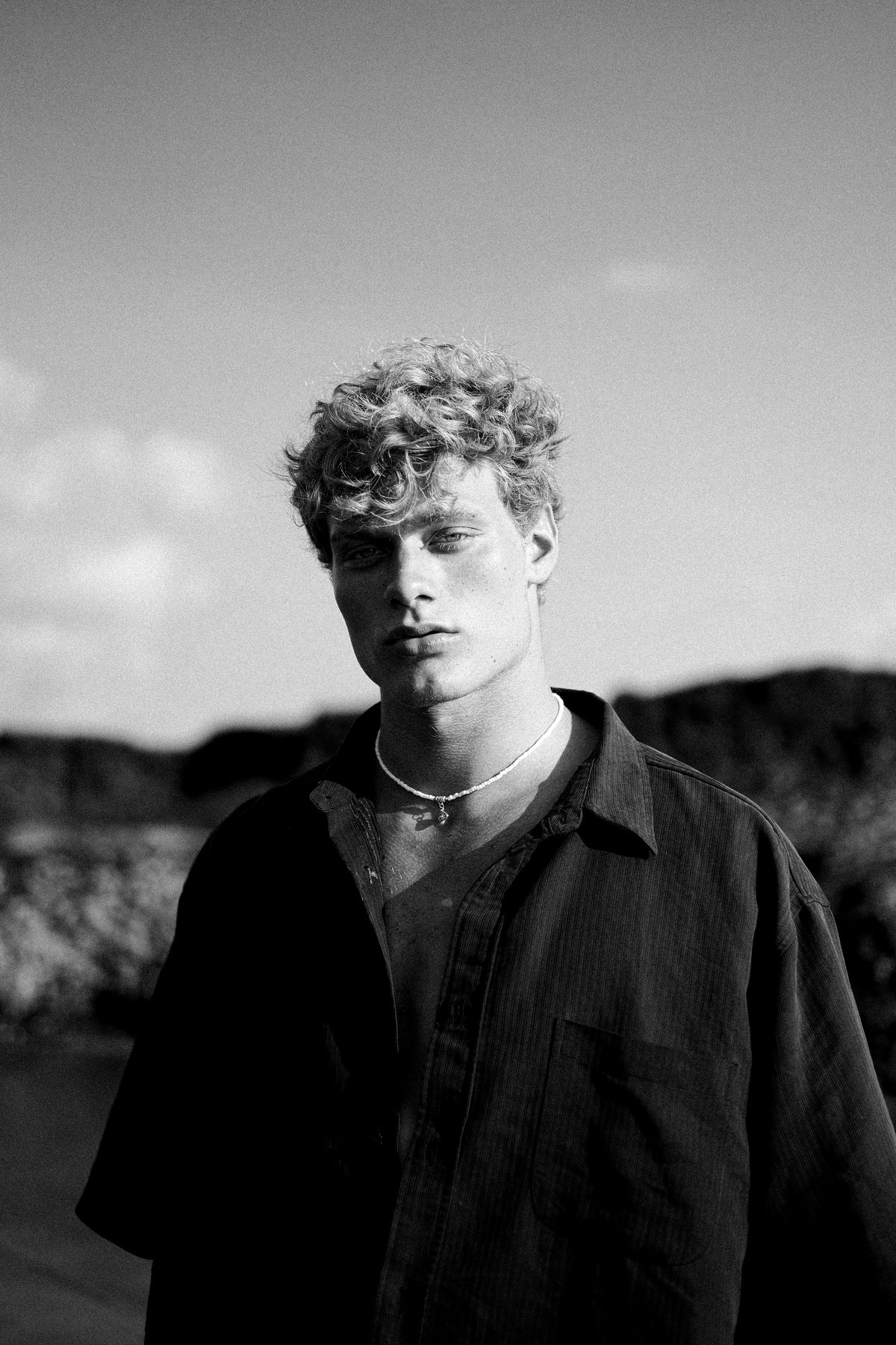 Black and white portrait of a young man with curly hair in an open shirt