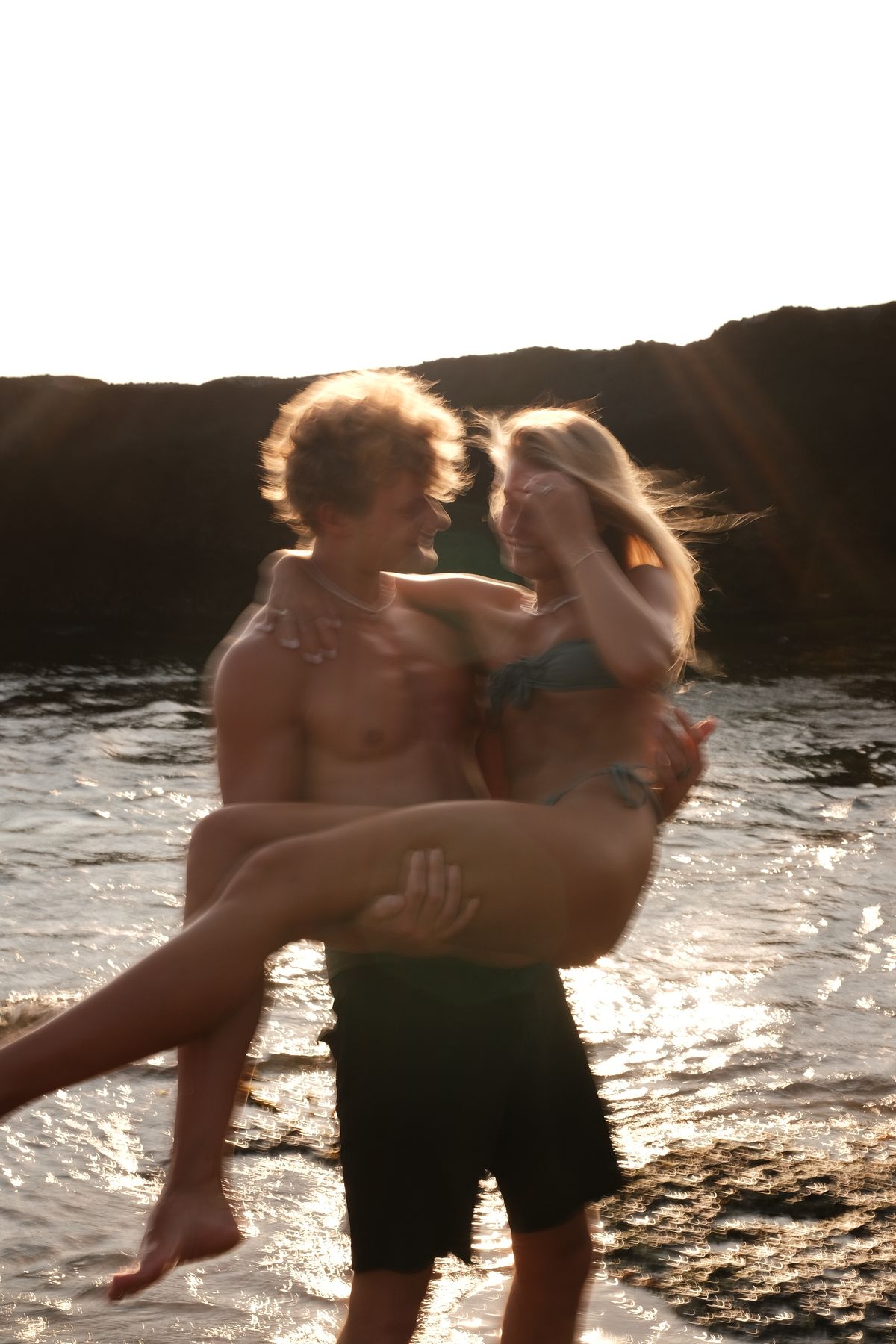 Man carrying a woman through shallow water at sunset