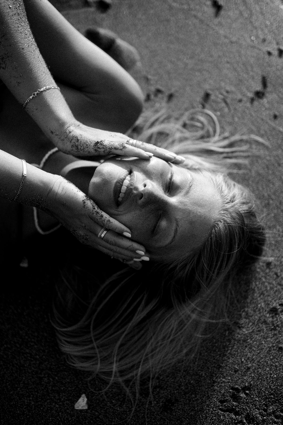 Black and white shot from above of a woman lying in the sand, hands over her face