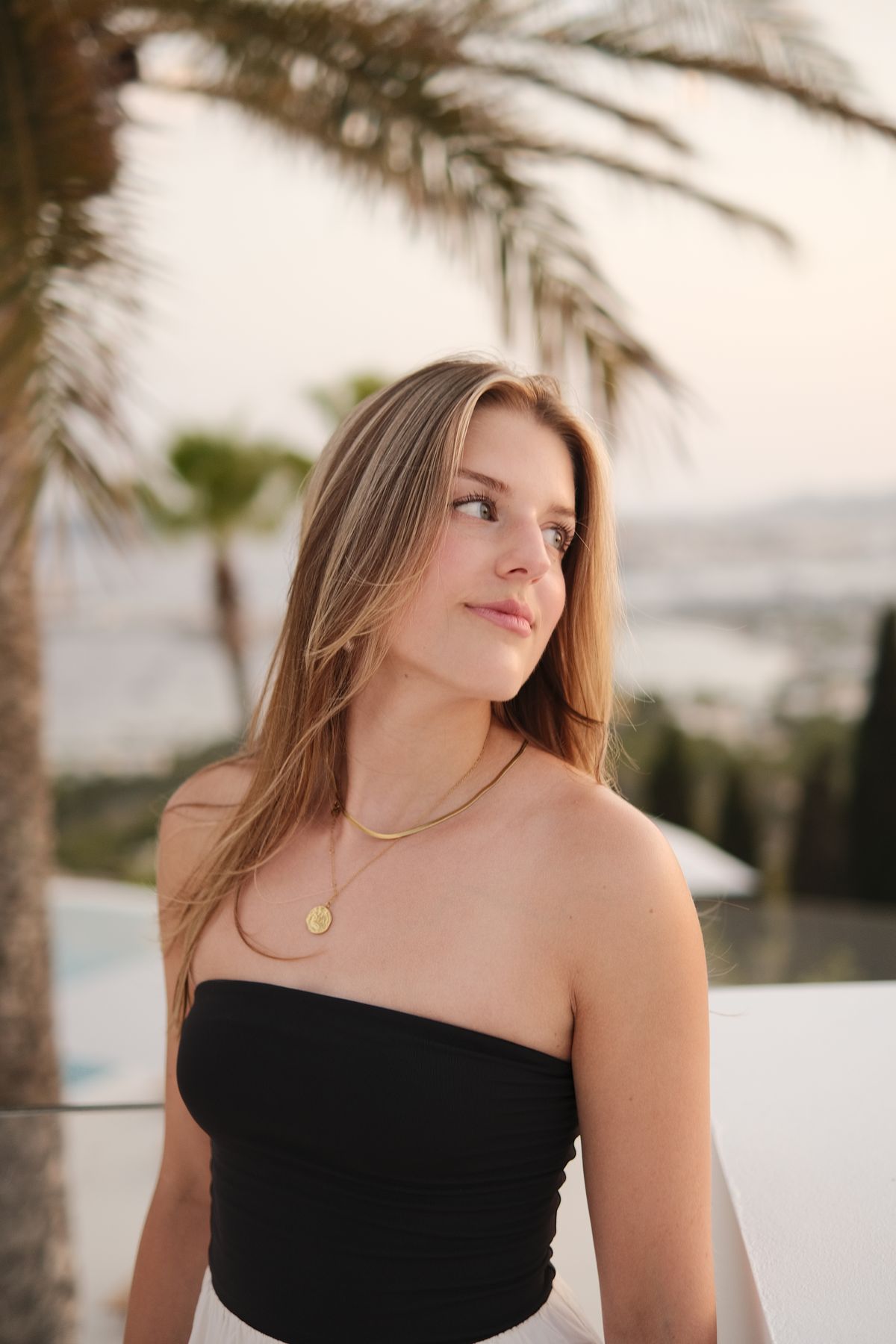 Woman in a black strapless top under a palm tree at golden hour
