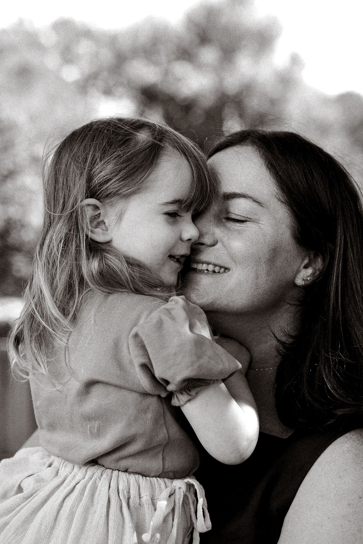 Black and white portrait of a mother and her small daughter, cheeks together, laughing