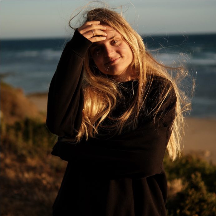Woman with wind-blown golden hair smiling on a coastal bluff at sunset
