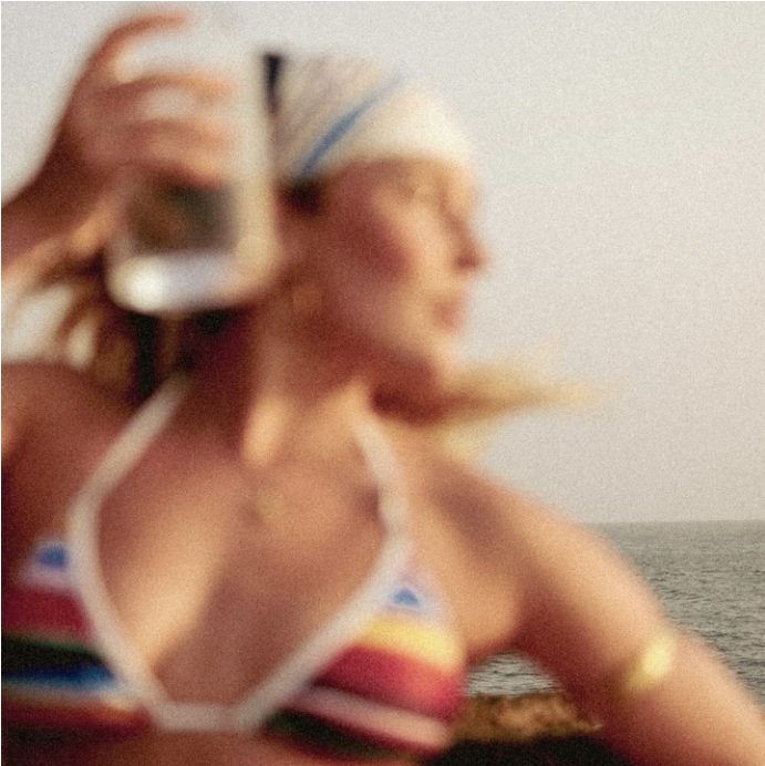 Blurred close-up of a woman in a headscarf and striped bikini holding a glass by the sea
