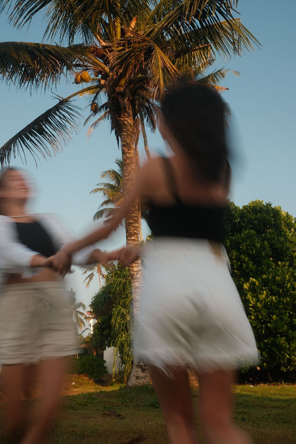 Two women spinning around holding hands under palm trees