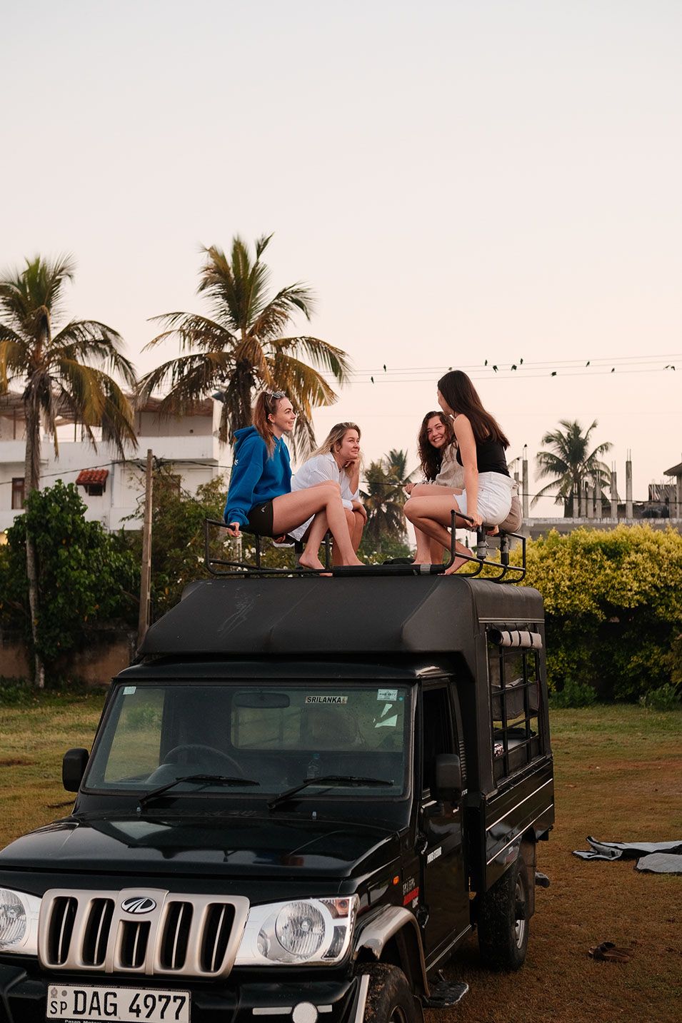 Three women sitting on the roof of a jeep under palm trees