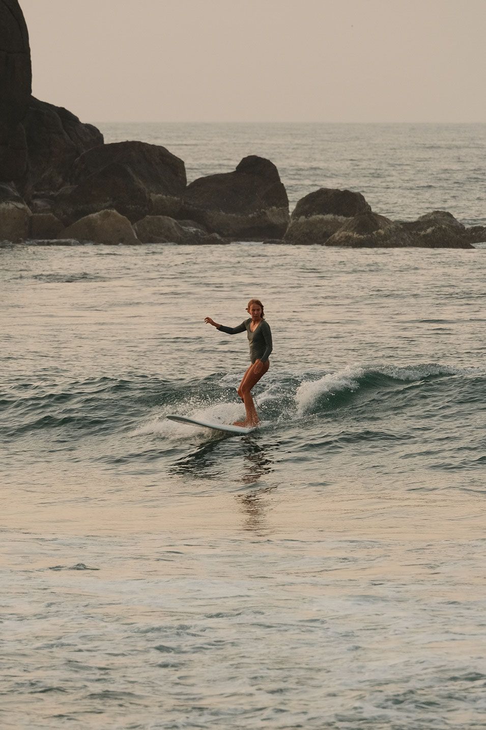 Surfer riding a small wave in front of dark rocks