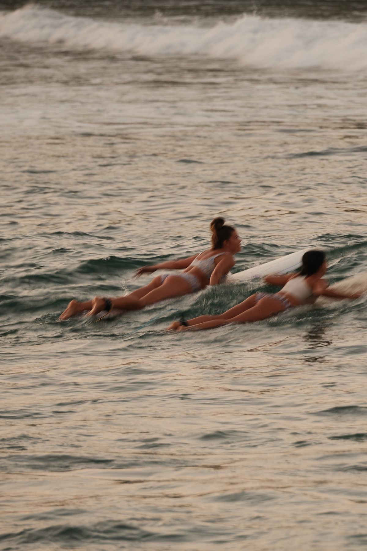 Two women paddling out on their boards side by side