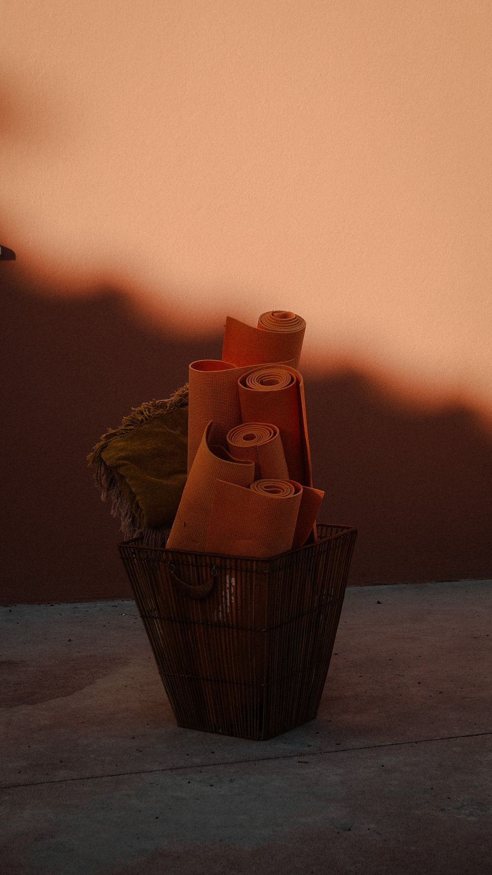 Rolled yoga mats in a basket against a terracotta wall