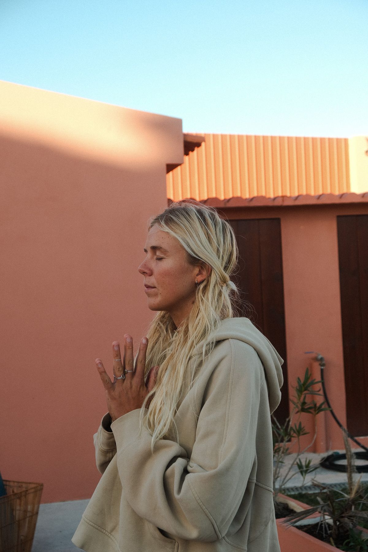 Blonde woman in a hoodie with her hands in prayer, eyes closed