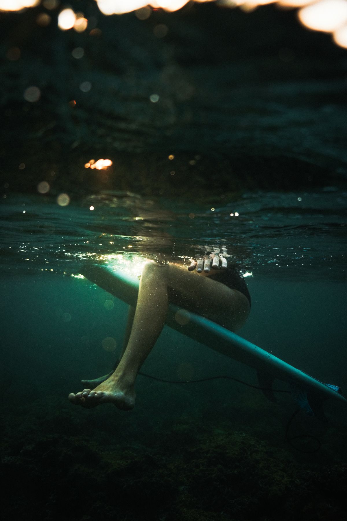 Underwater shot of a surfer's legs dangling from a board, light breaking through the surface
