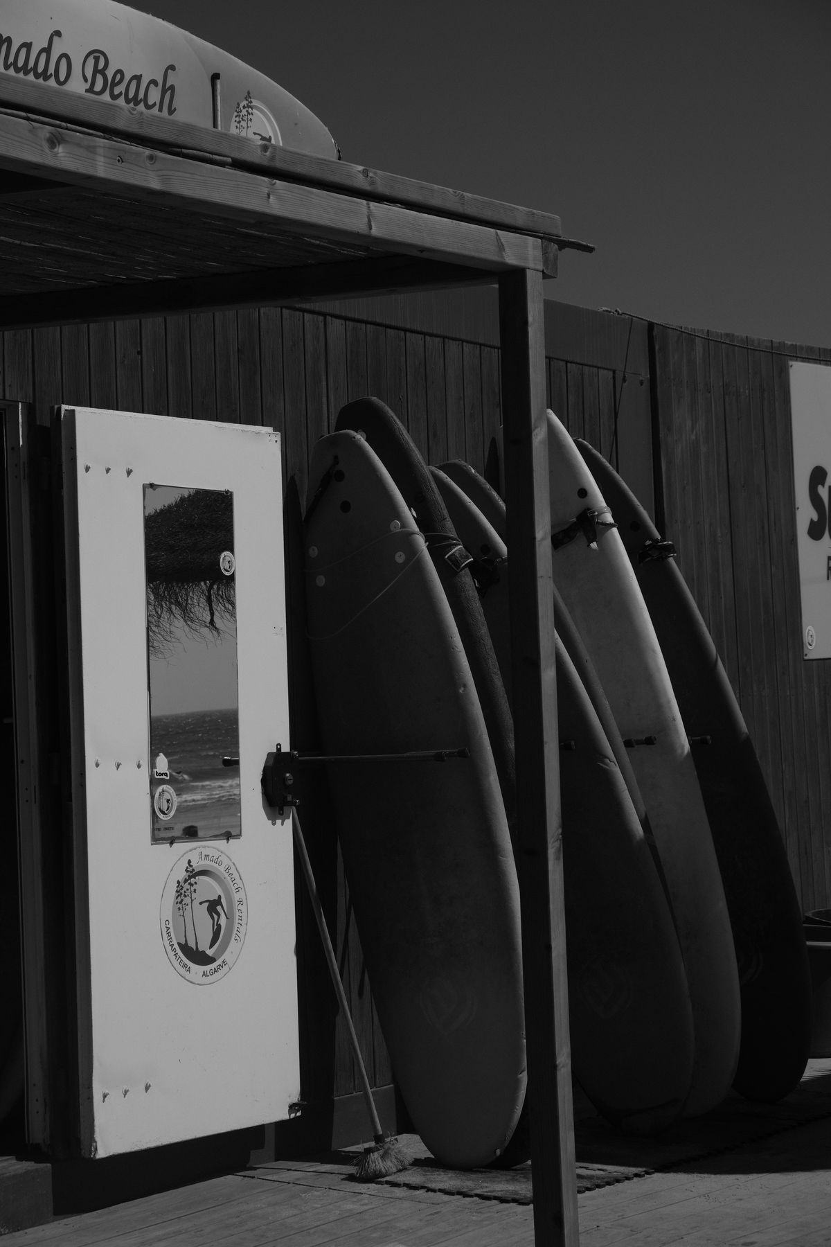 Black and white shot of surfboards stacked against a beach hut