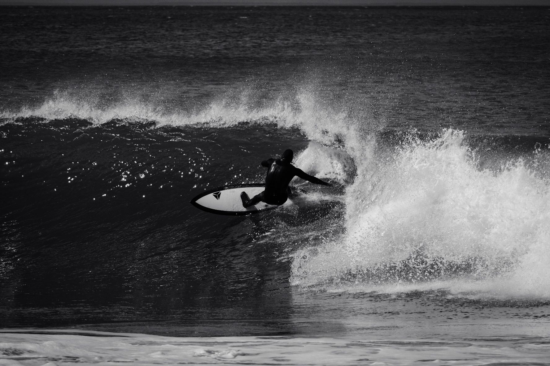 Black and white shot of a surfer carving a turn, spray flying off the wave