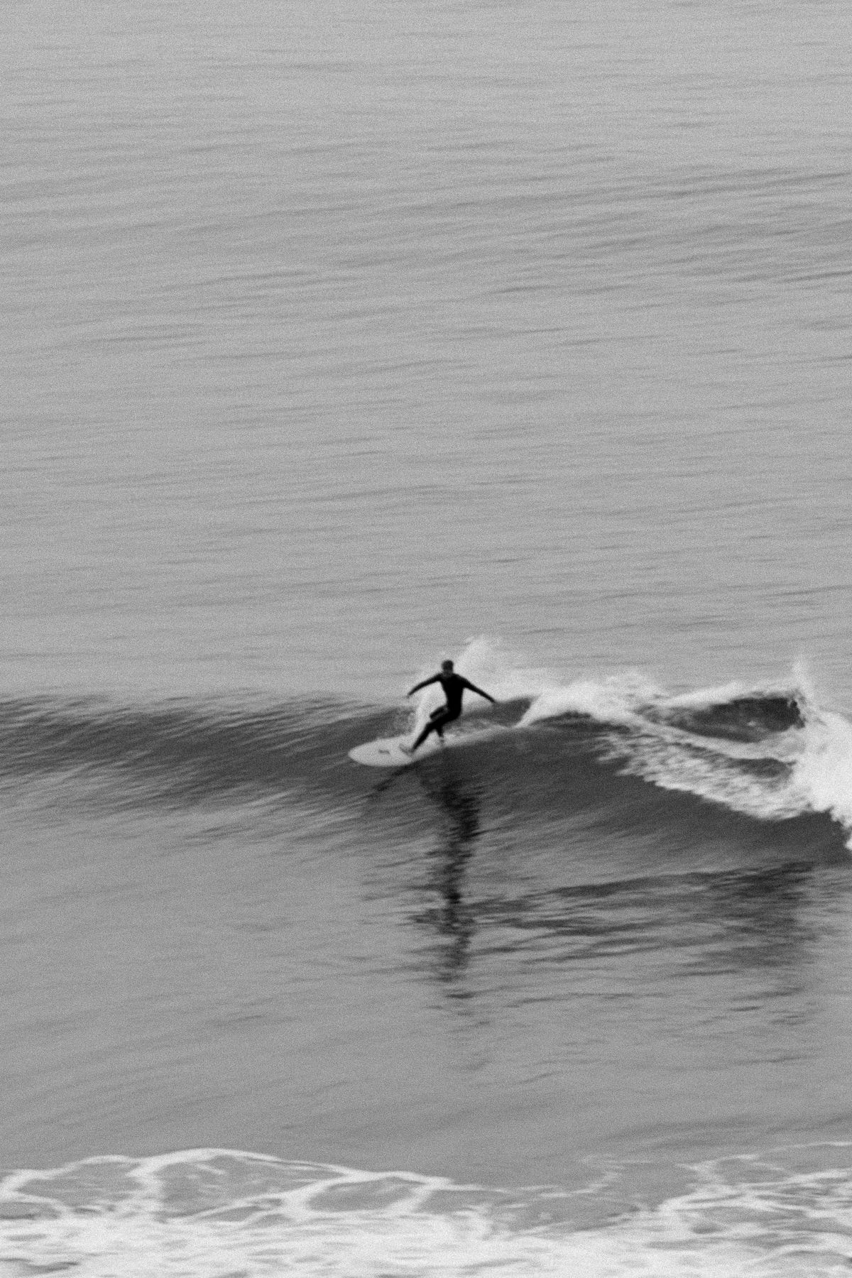 Black and white shot of a surfer riding a long, small wave