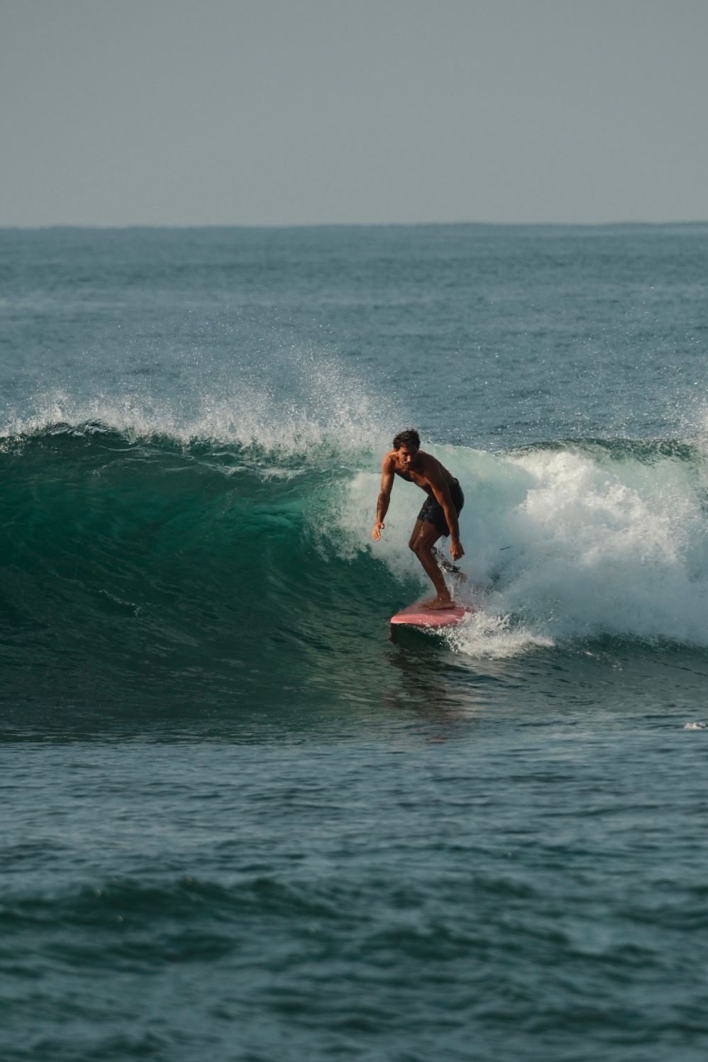 Surfer riding a pink board along a turquoise wave