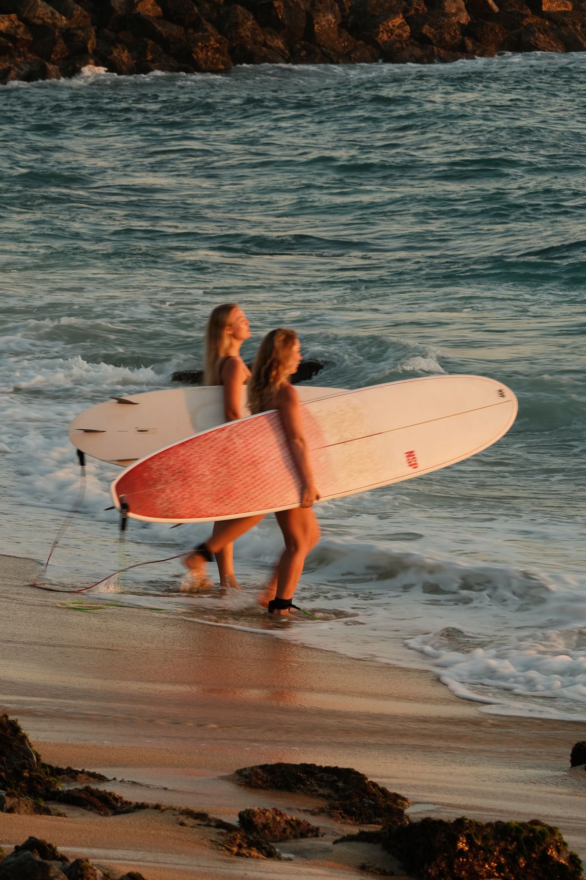 Two women walking out of the sea with their longboards at sunset