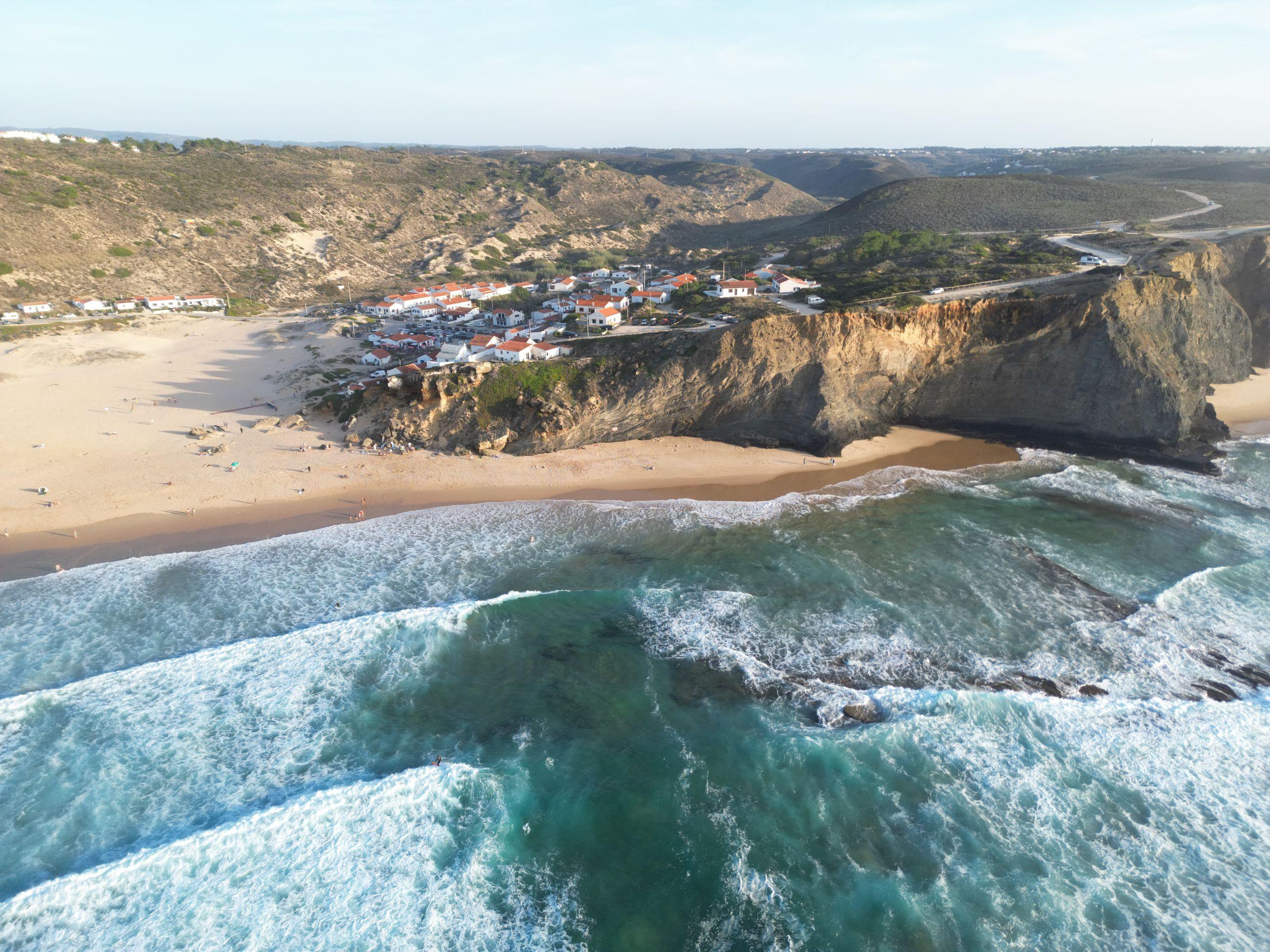 Drone shot of a cliff, a beach and a village above breaking Atlantic waves