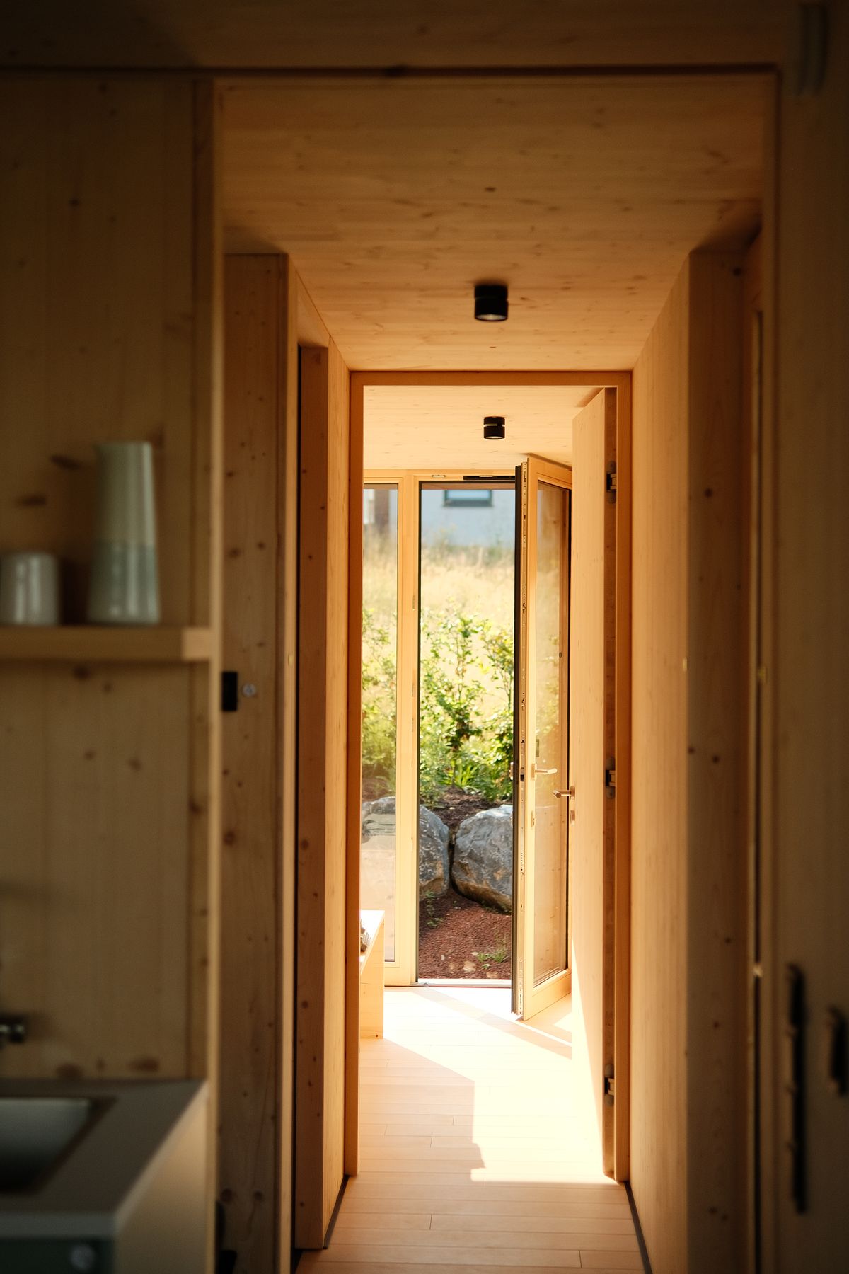 Wooden cabin hallway leading to a glass door and the garden