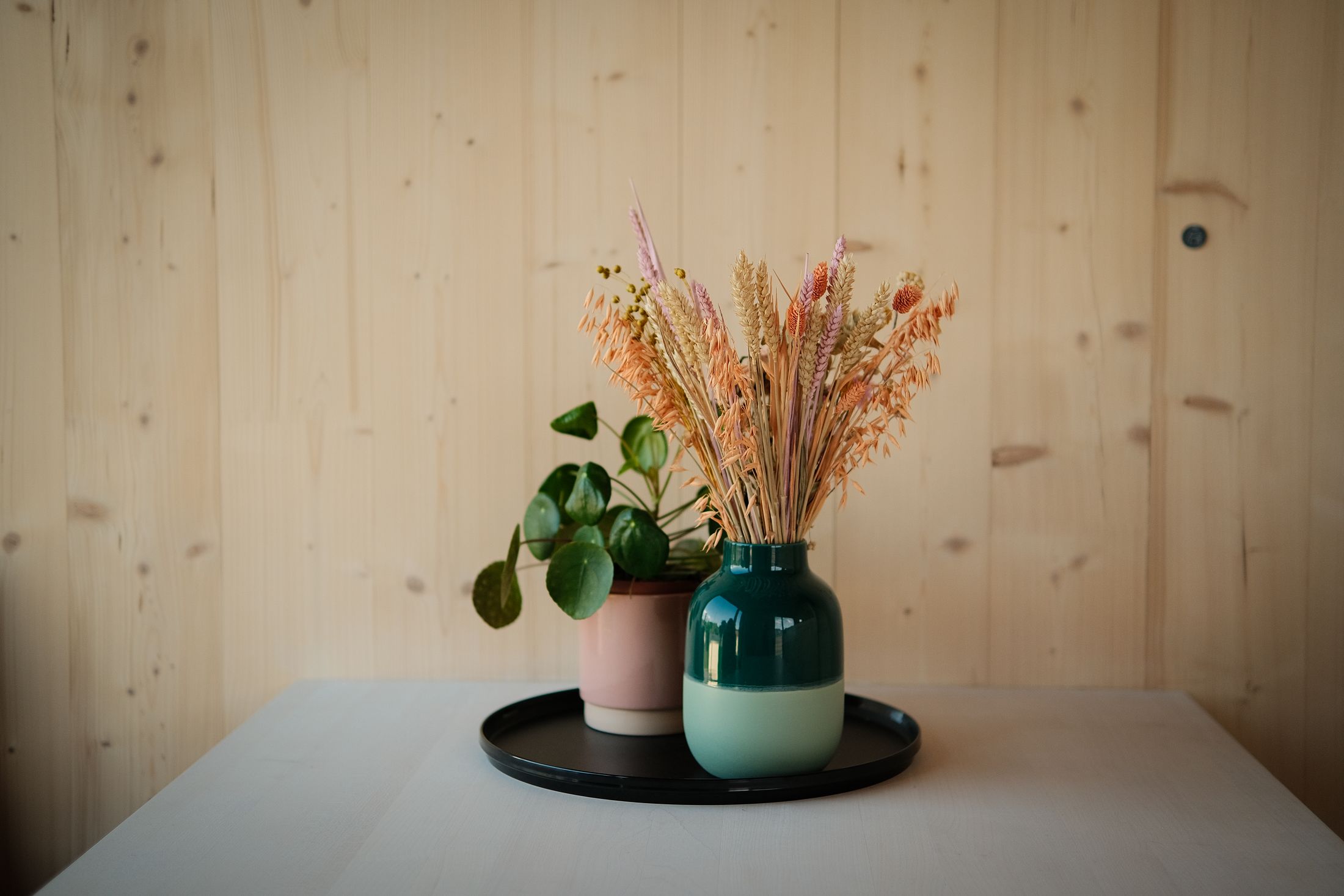 Dried flowers and a vase on a white table against a pale wood wall