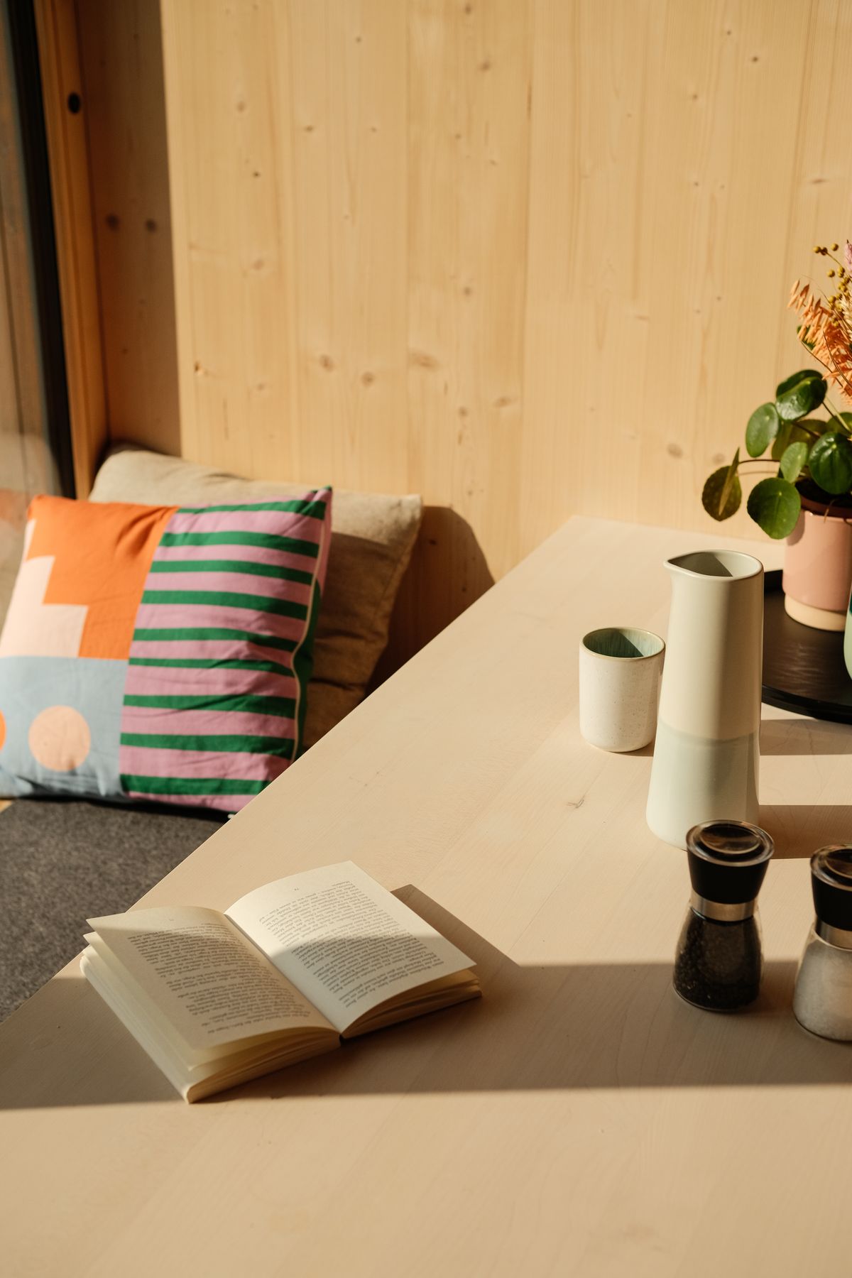 Book, cushions and ceramics on a sunny window seat in a wooden cabin