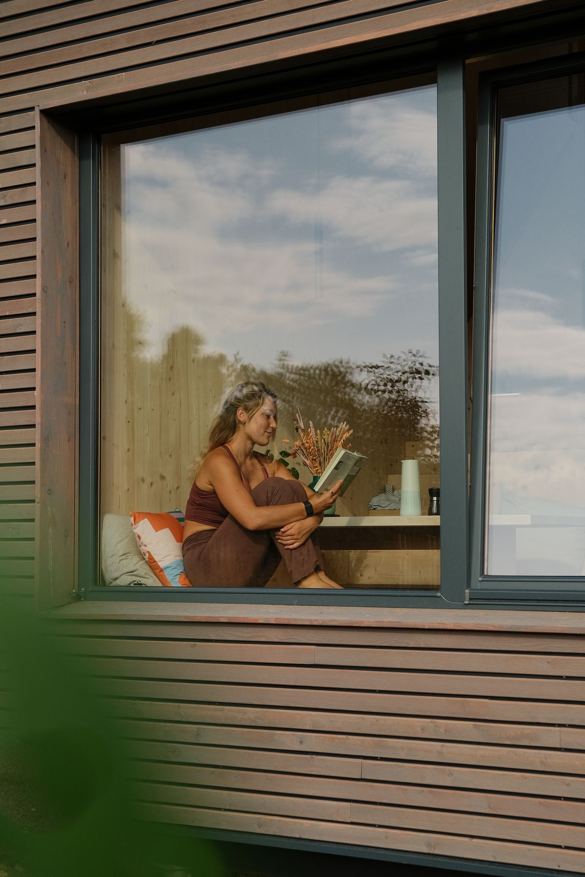Woman reading inside the cabin, seen through the window from outside