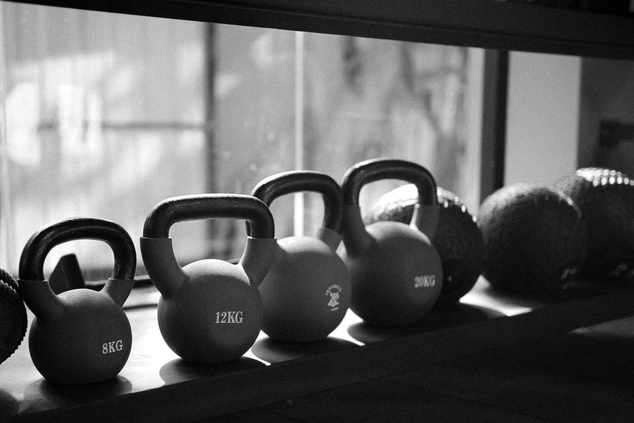 Black and white shot of kettlebells and medicine balls on a shelf by the window