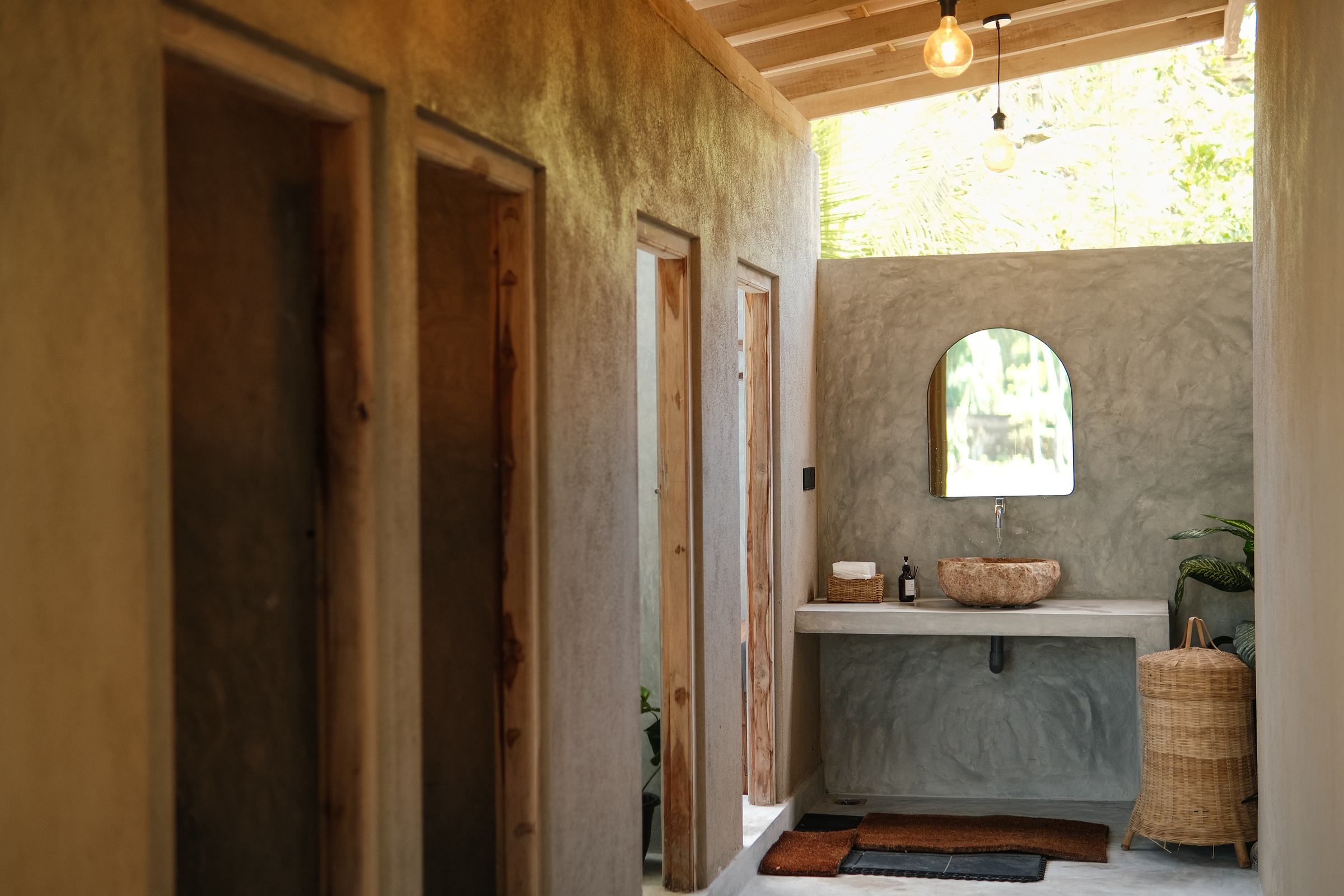 Clay-walled corridor with wooden doors, a hanging bulb and an arched mirror at the end