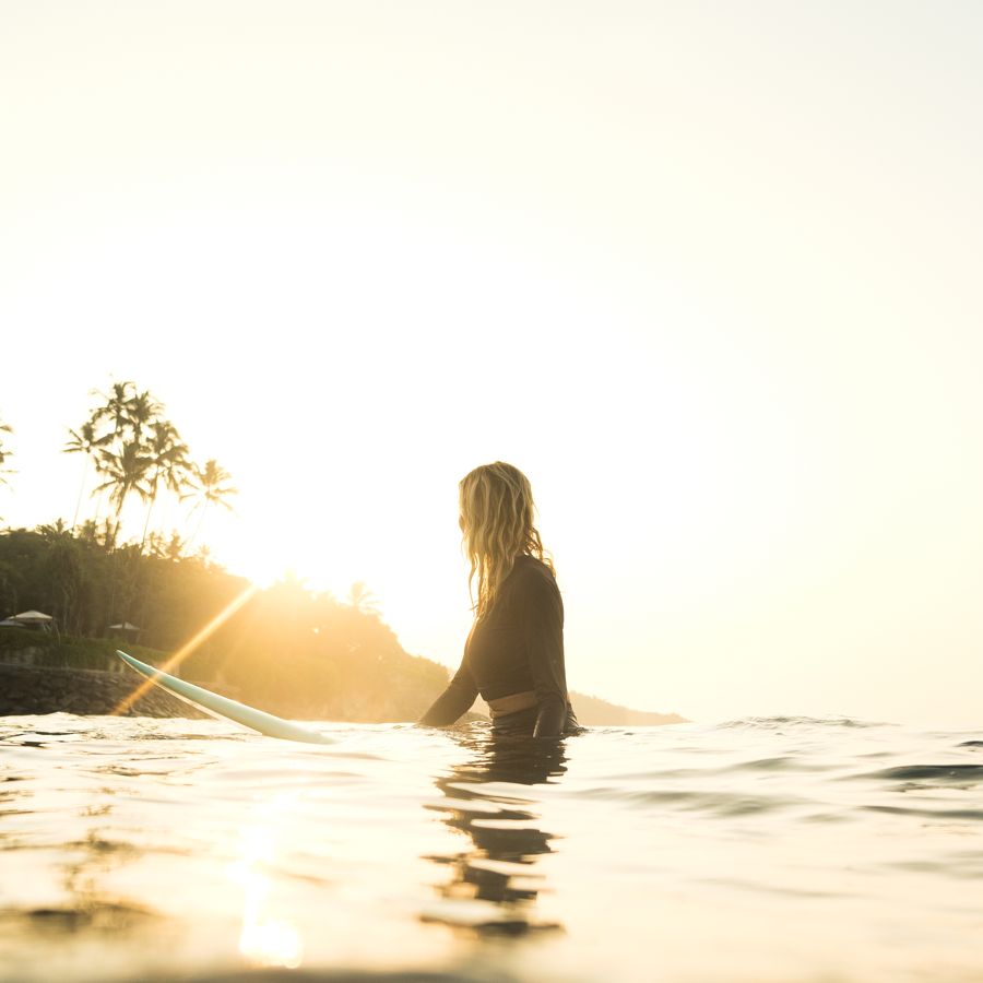 Surfer sitting on a board in glowing sunset water, palm trees behind